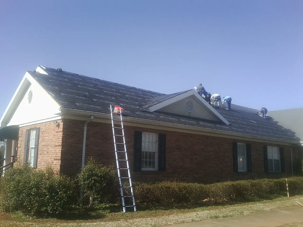 Crew tearing shingles off a brick ranch roof with a ladder set — Emergency Roof Repair work by our crew in Alma
