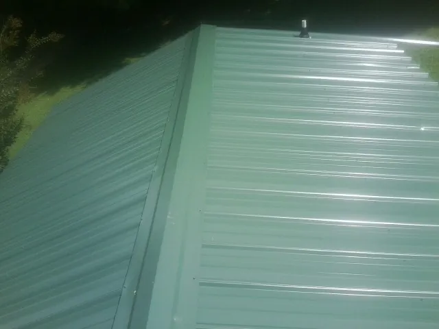 New green metal panels meeting at the ridge of a roof — Flat Roof Repair work by our crew in Alma