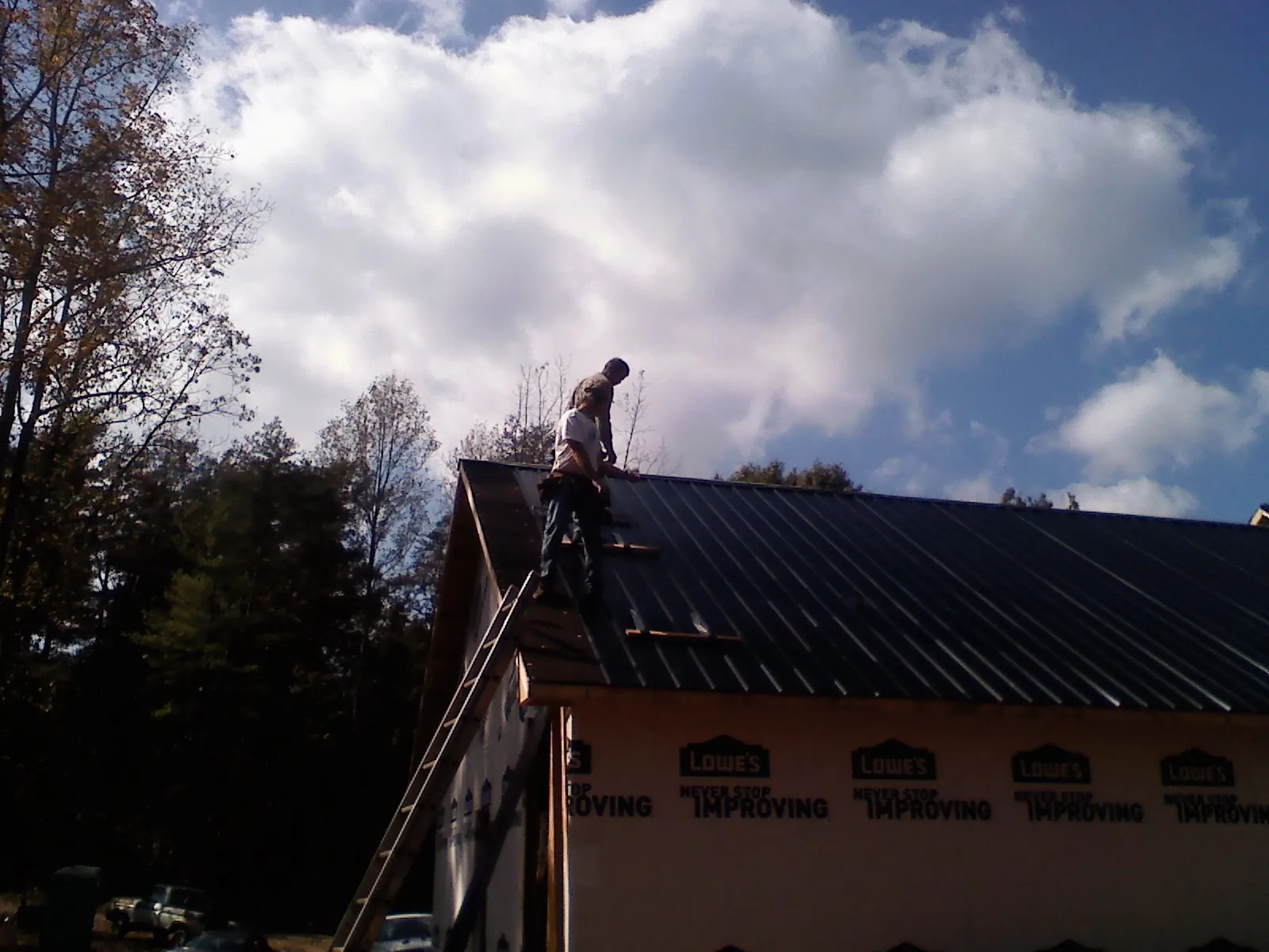 Roofer fastening dark metal panels high against a cloudy sky, from a Roof Inspection job in Alma