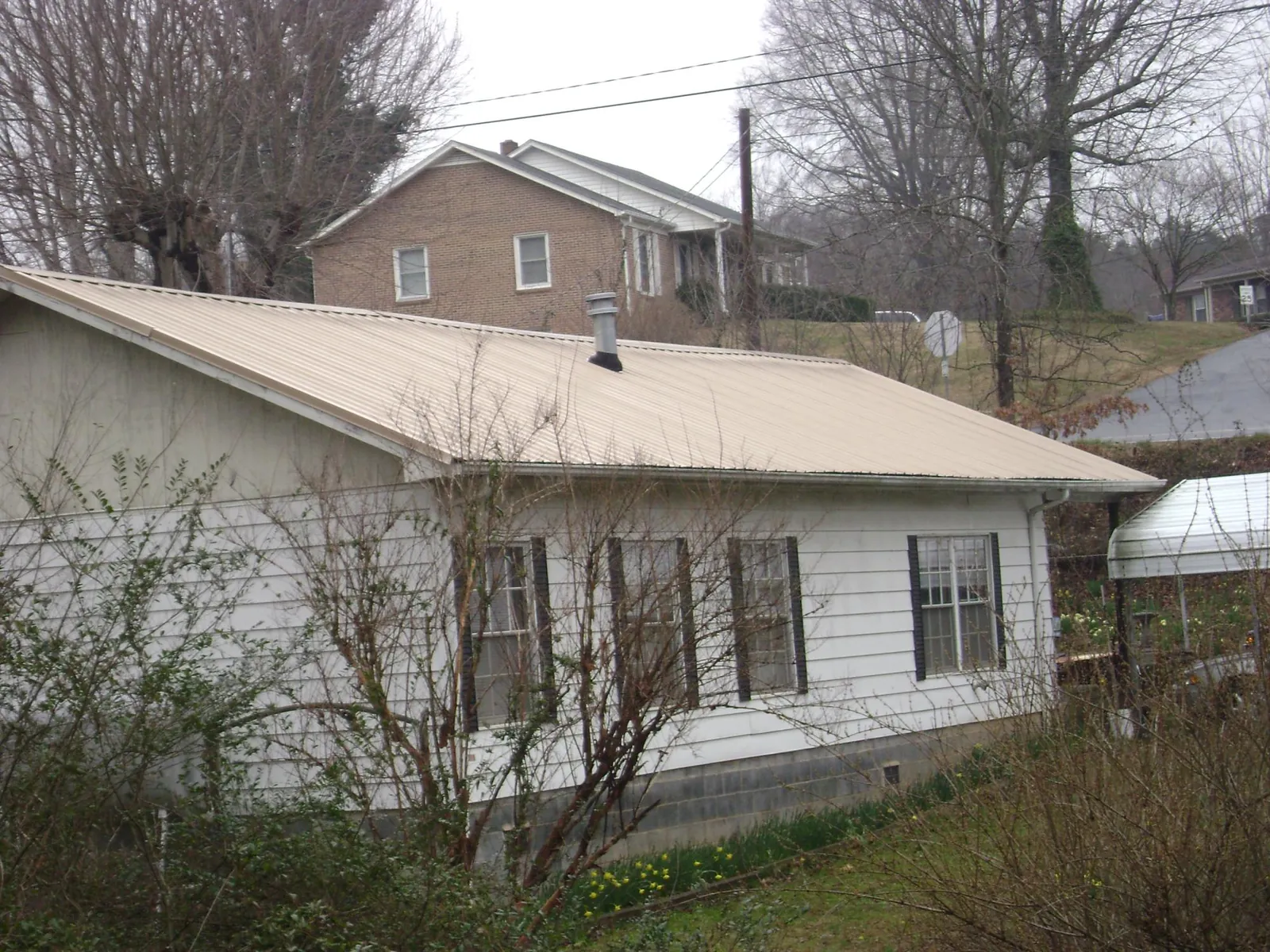 Tan metal roof on a white sided house set into a hillside — Commercial Roofing by Roofing Brothers in Alma
